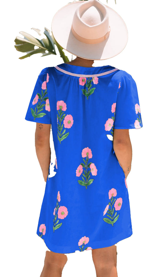 Model wearing a blue floral mini dress with pink flowers, set against a tropical background
