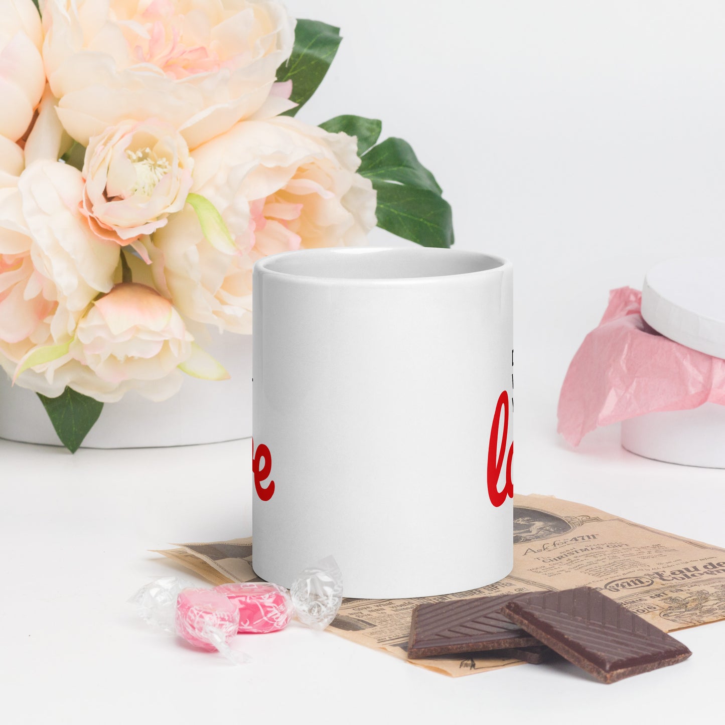 White do what you love coffee mug with red text on table next to flowers chocolate and candy