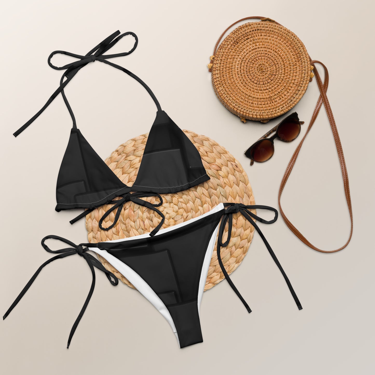 Sustainable black string bikini set laid flat with round straw bag and sunglasses