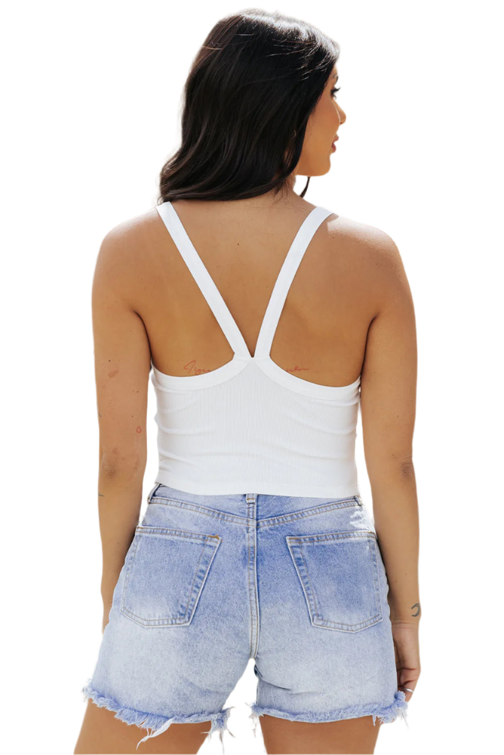 Back view of woman wearing a white ribbed cropped cami top paired with light denim shorts