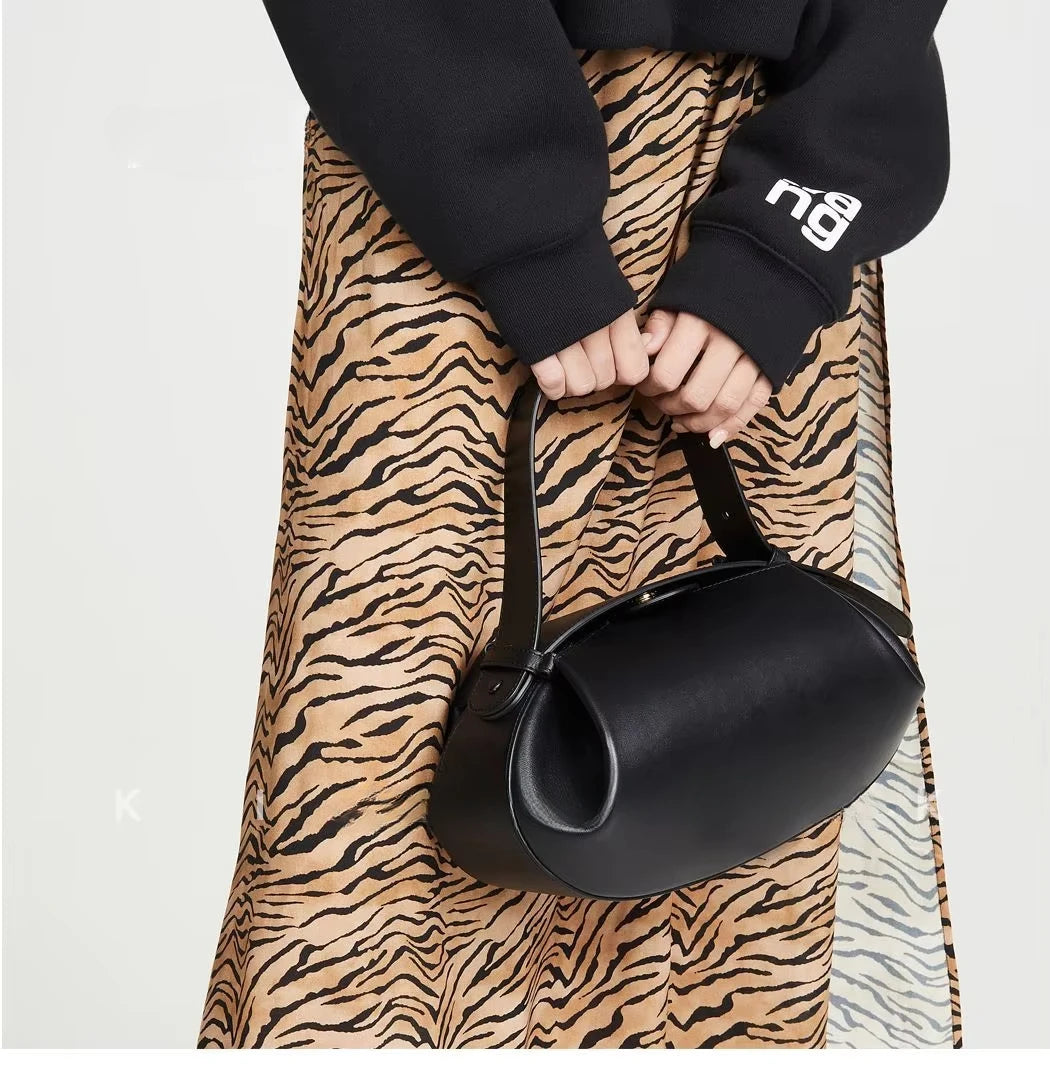 Stylish black women's crossbody round bag held by a model in a tiger print skirt
