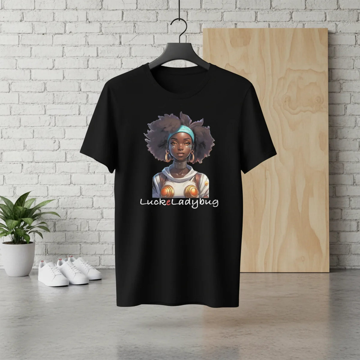 Black t-shirt with a graphic design of a woman with an afro and 'Luckyladybug' text, hanging against a white brick wall.