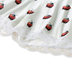 Close-up of a white garment with a ladybug print and lace trim.
