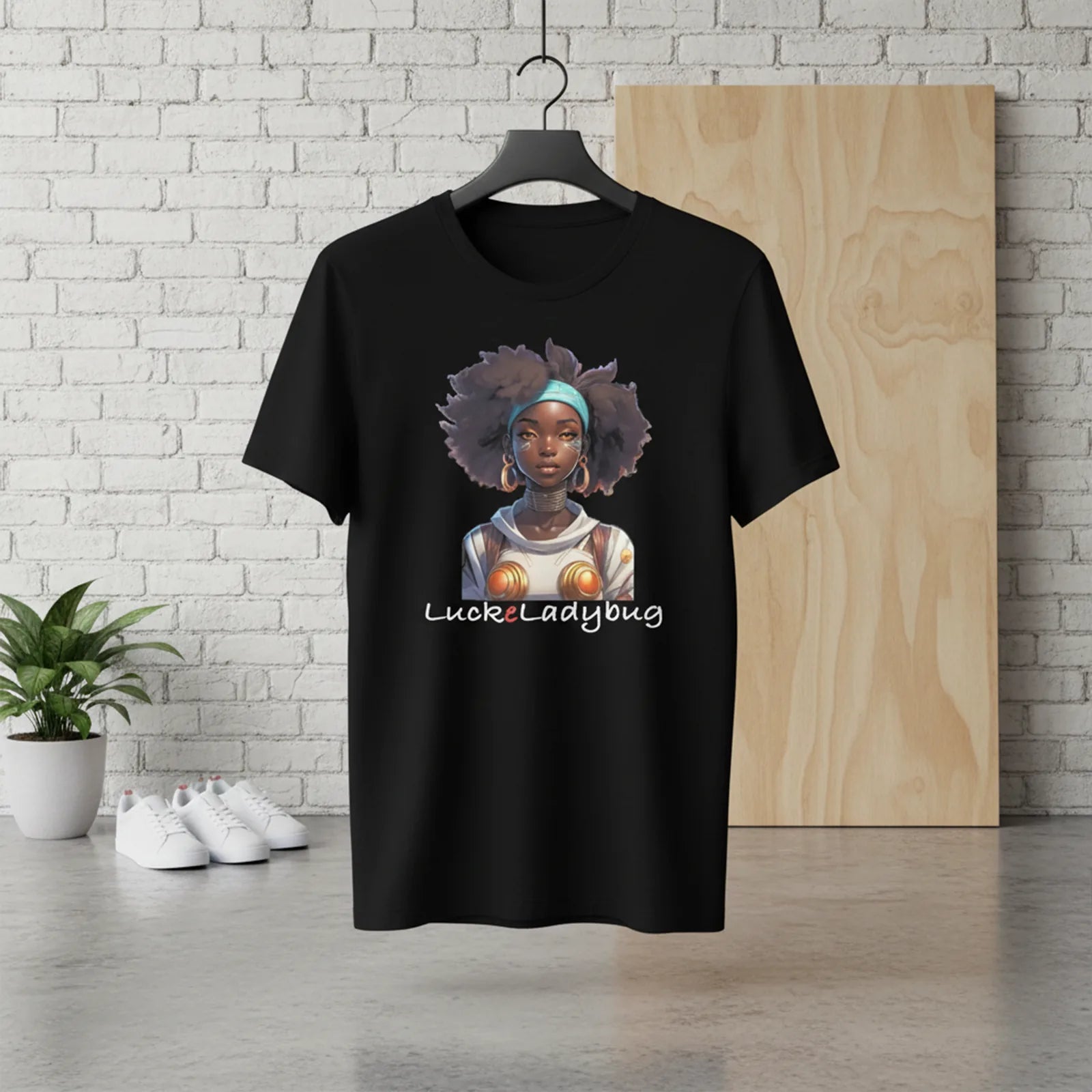 Black t-shirt with a graphic design of a woman with an afro and 'Luckyladybug' text, hanging against a white brick wall.