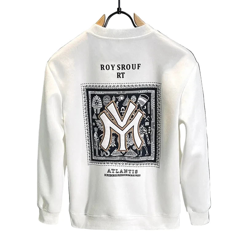 A white crewneck sweatshirt hanging on a black hanger against a dark gray wall. The back of the sweatshirt features a large graphic print with a black and white patterned border, a large stylized 'M' logo in the center, and text reading 'ROY SROUF RT' above and 'ATLANTIC' below.