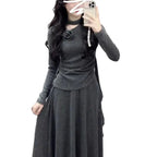 Person wearing a dark gray long-sleeve top and skirt against a textured wall.