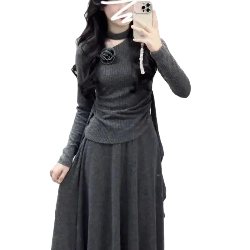Person wearing a dark gray long-sleeve top and skirt against a textured wall.