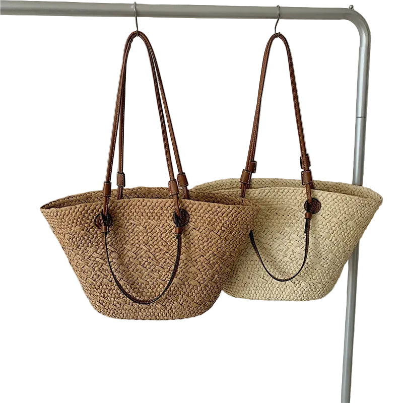 Two woven handbags with brown handles hanging on a rack against a plain background.