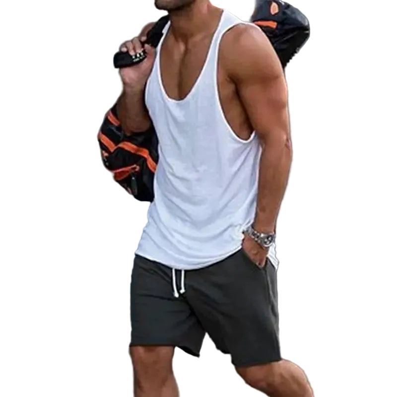 Man wearing a white tank top and black shorts walking outdoors.