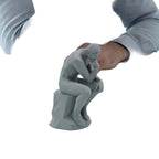 Gray 'Thinker' sculpture on a desk with a person in a gray shirt.