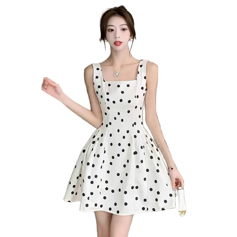 Woman wearing a white dress with black polka dots in an indoor setting.