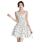 Woman wearing a white dress with black polka dots in an indoor setting.