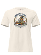 An off-white short-sleeve crewneck t-shirt featuring a vintage-style graphic of a lion wearing a blue cap and sitting at a desk with books, surrounded by the text 'UNBOTHERED & BRIGHT & BRAVE' and 'STUDYING TO KEEP IT SIMPLE'.