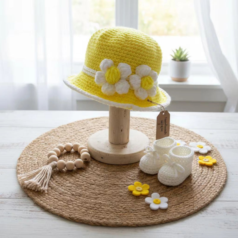 Handmade yellow crochet baby hat with flower decorations, displayed with matching baby booties and accessories