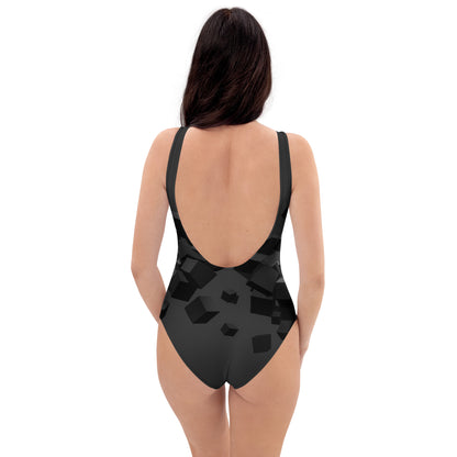 Back view of model wearing LuckeLadybug black pattern one-piece swimsuit with geometric cube print and low scoop back