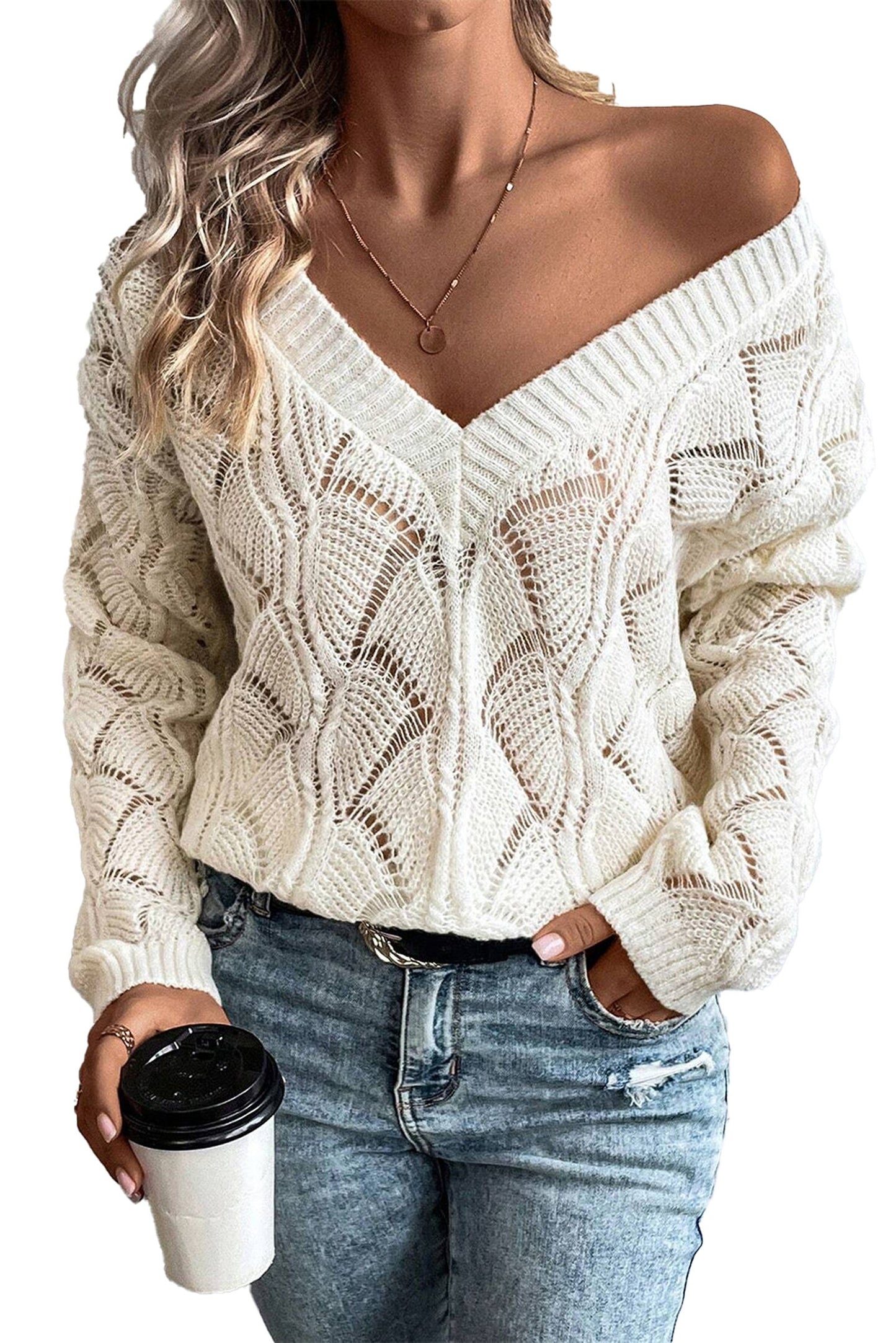 Woman wearing a white open-knit sweater with v-neck design, featuring a casual look and holding a coffee cup