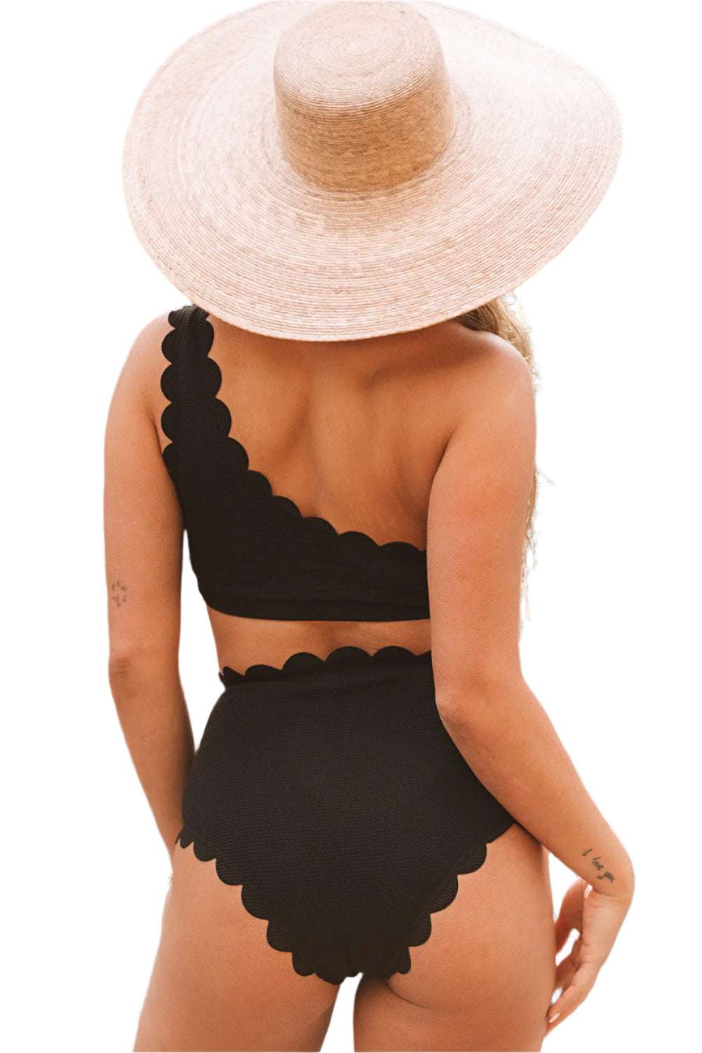 Back view of black scalloped one-shoulder bikini with high-waist bottoms worn with a wide-brim straw hat