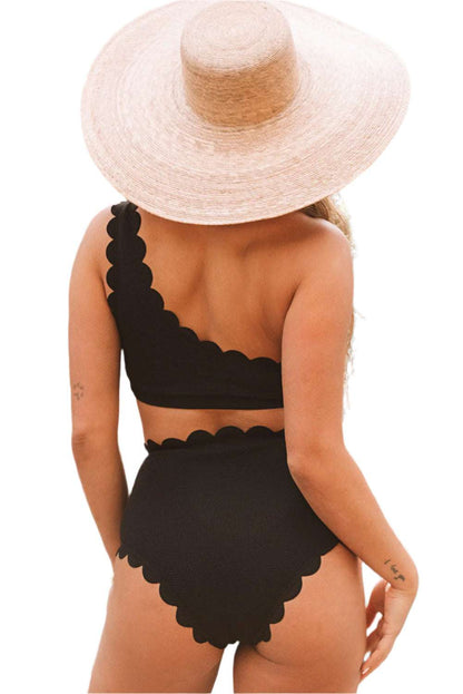 Back view of black scalloped one-shoulder bikini with high-waist bottoms worn with a wide-brim straw hat