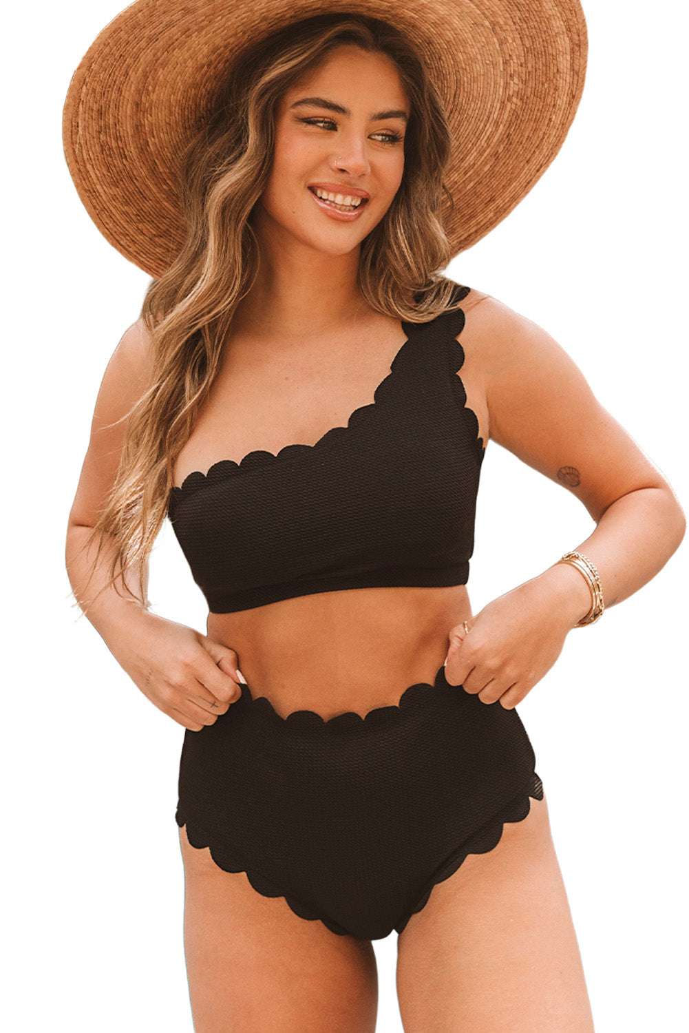 Black scalloped one-shoulder bikini with high-waisted bottoms worn by a woman with a wide-brimmed hat