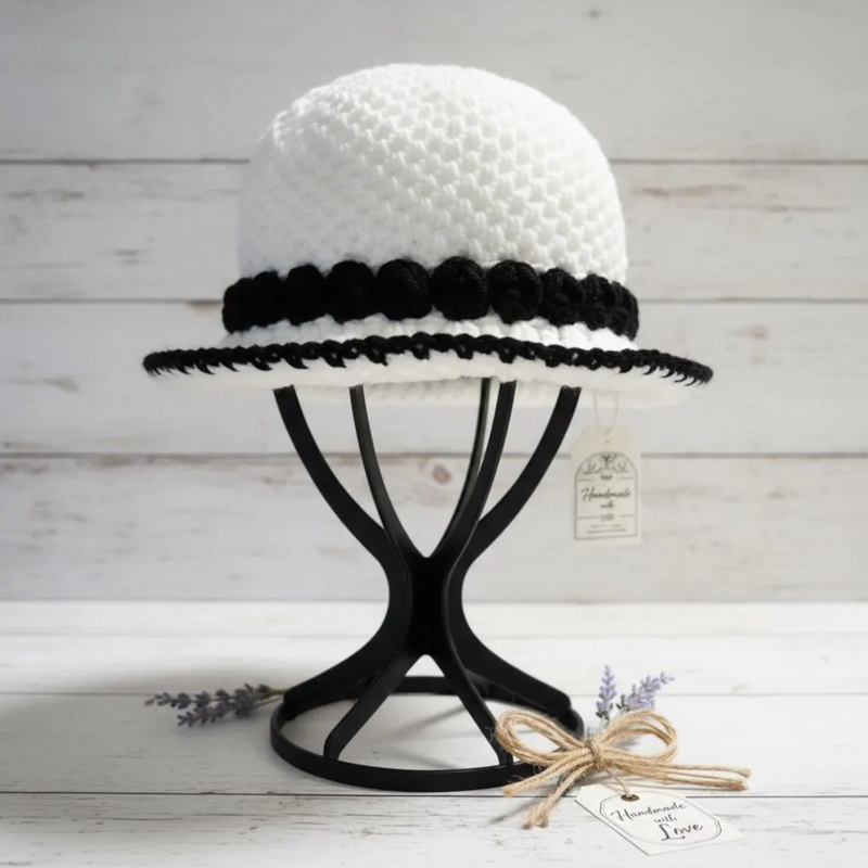 White Crochet Bucket Hat with Black Trim on a Display Stand by ThreadsByHannah, perfect for fashionable styles