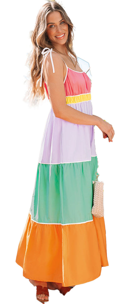 Smiling model in a multicolor colorblock maxi dress with tie shoulders and straw bag in tropical garden