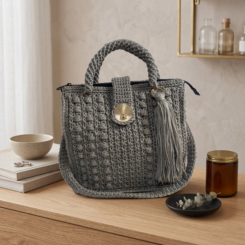 Stylish gray coach purse shoulder bag with braided handles and tassel detail on wooden surface