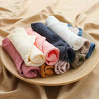 Assorted cotton washcloths in a variety of colors, neatly rolled on a wooden plate