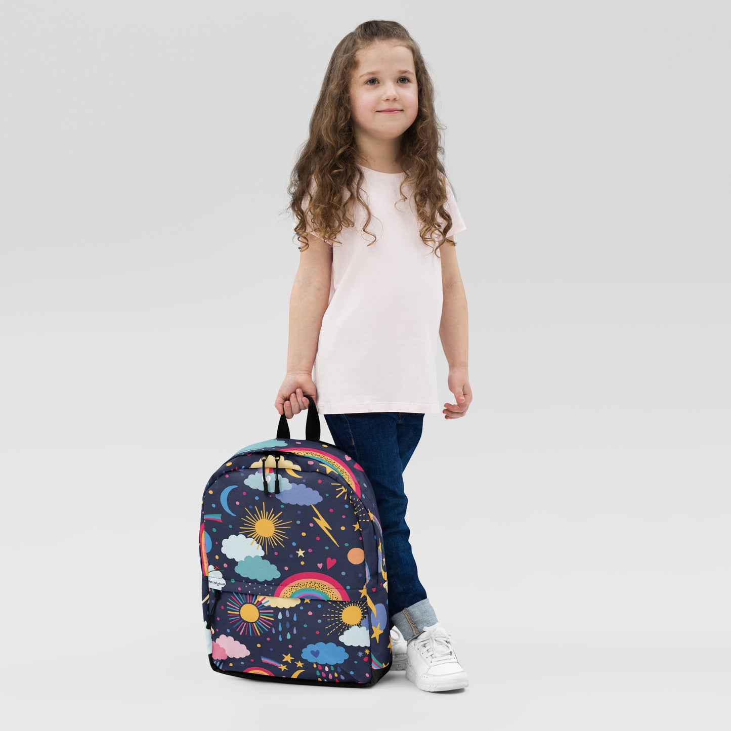 Cute cloud print backpack with colorful rainbows and stars held by young girl wearing pink shirt and jeans