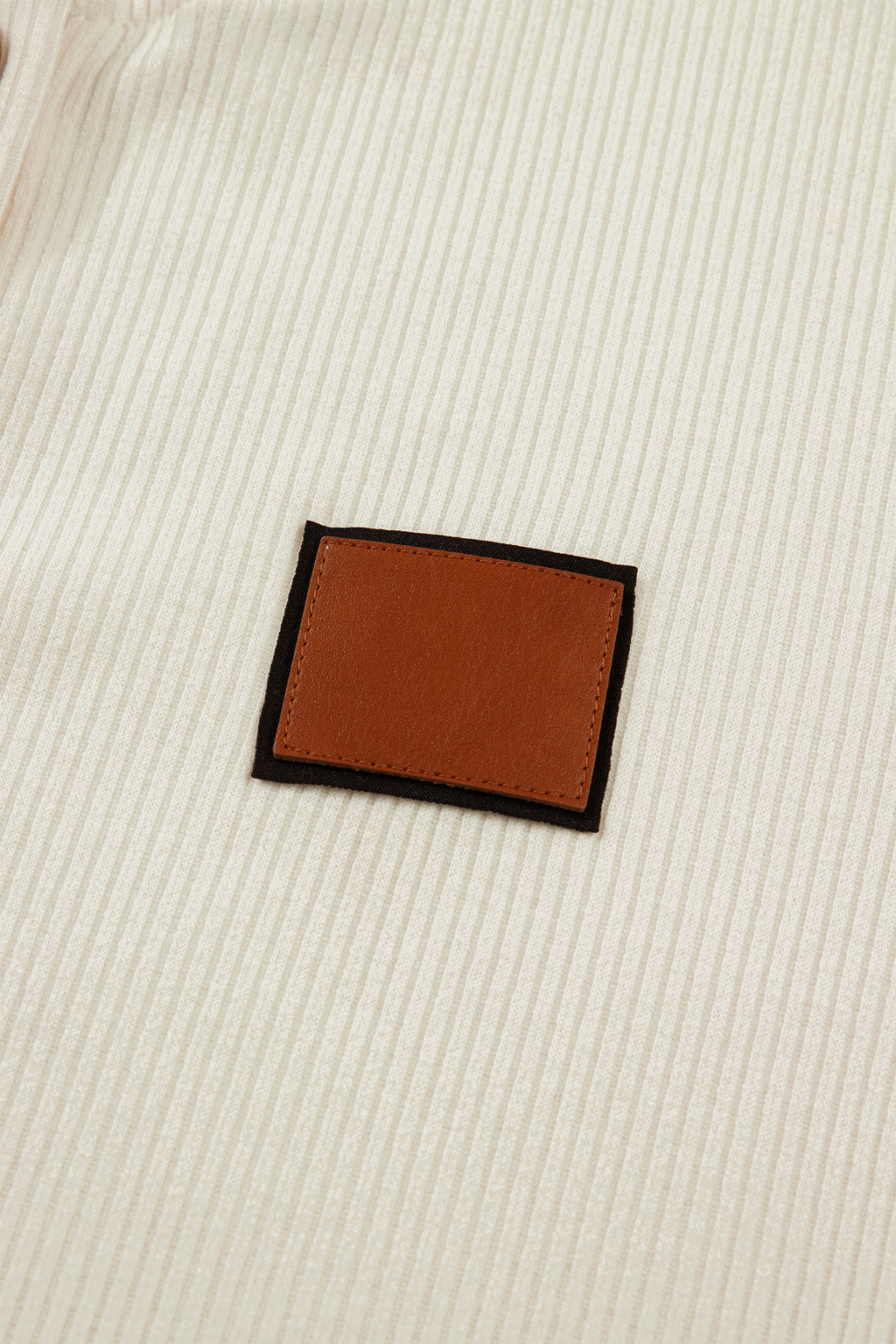 Close-up of a beige fabric with a leather patch, featured on a LuckeLadybug denim shirt