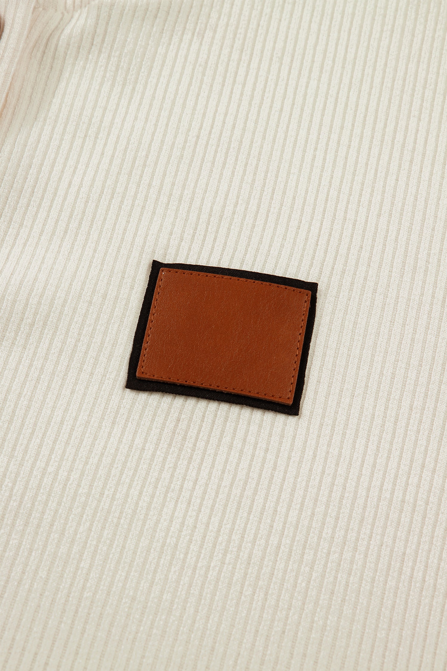 Close-up of a beige fabric with a leather patch, featured on a LuckeLadybug denim shirt