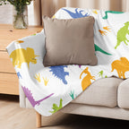 LuckeLadybug dinosaur sherpa blanket with colorful dinosaur patterns draped over a beige sofa