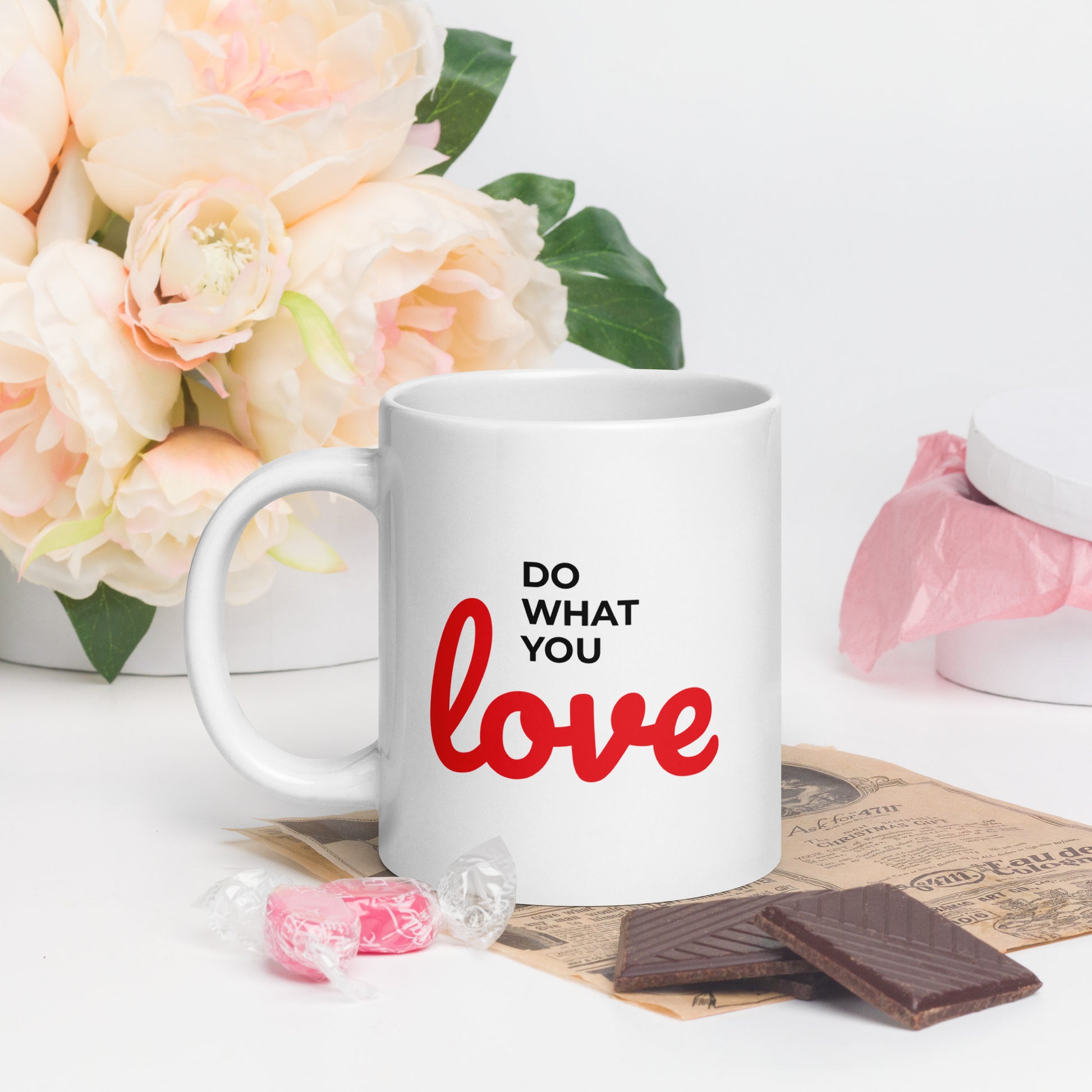 LuckeLadybug white ceramic do what you love coffee mug with red and black text next to flowers and chocolate