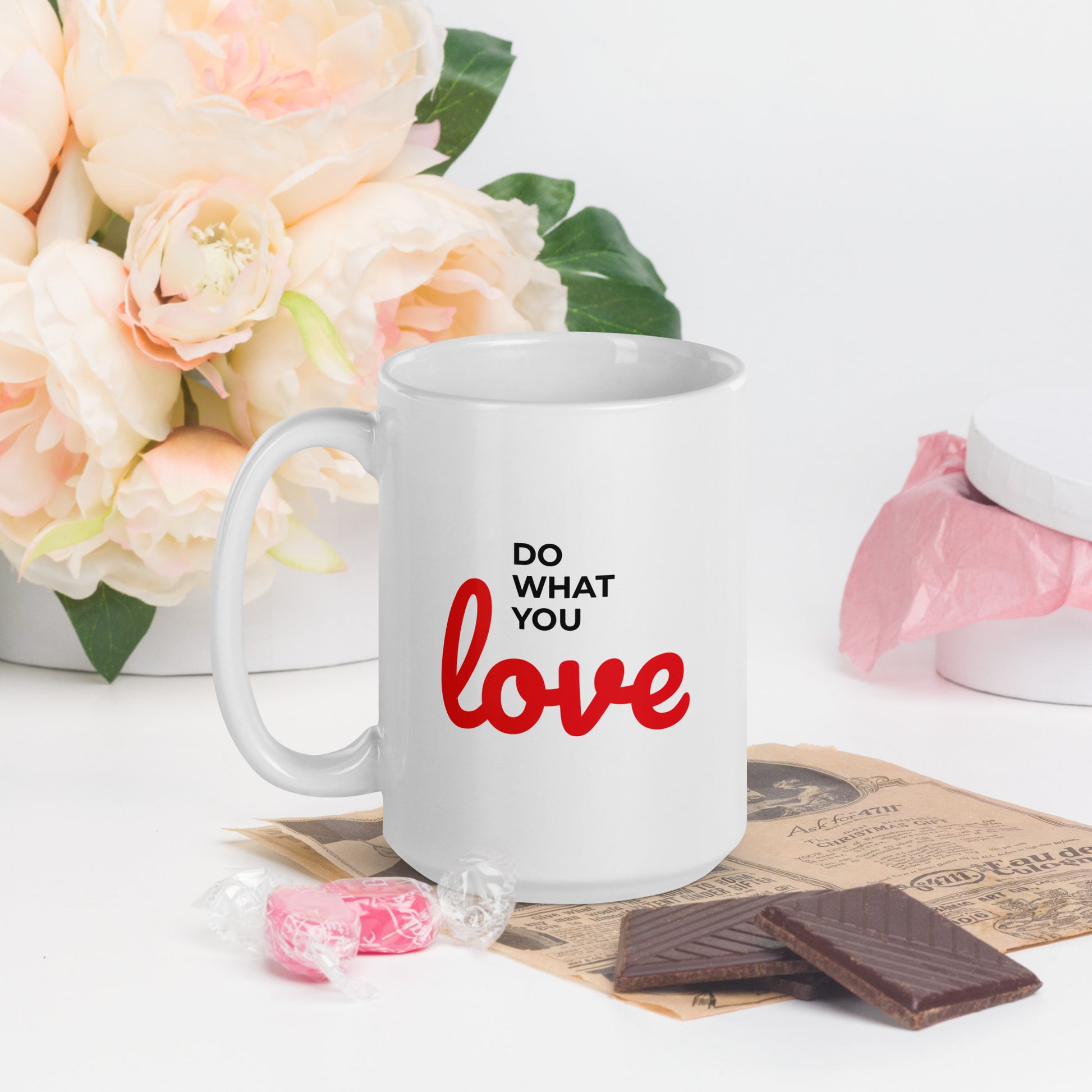 White do what you love coffee mug with red and black text on a table with flowers and chocolates