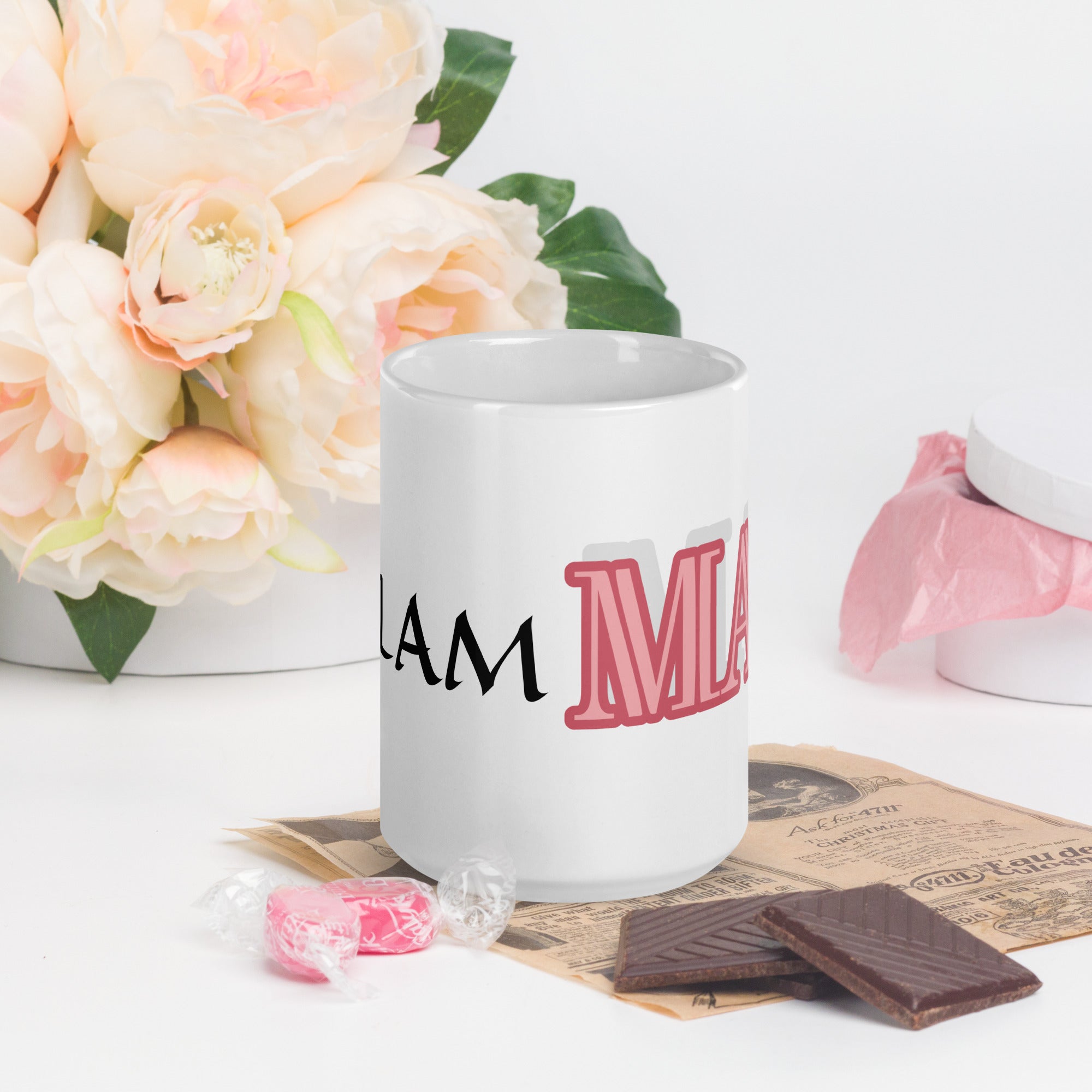 White mug with pink and black glam ma coffee mug text beside flowers and chocolates