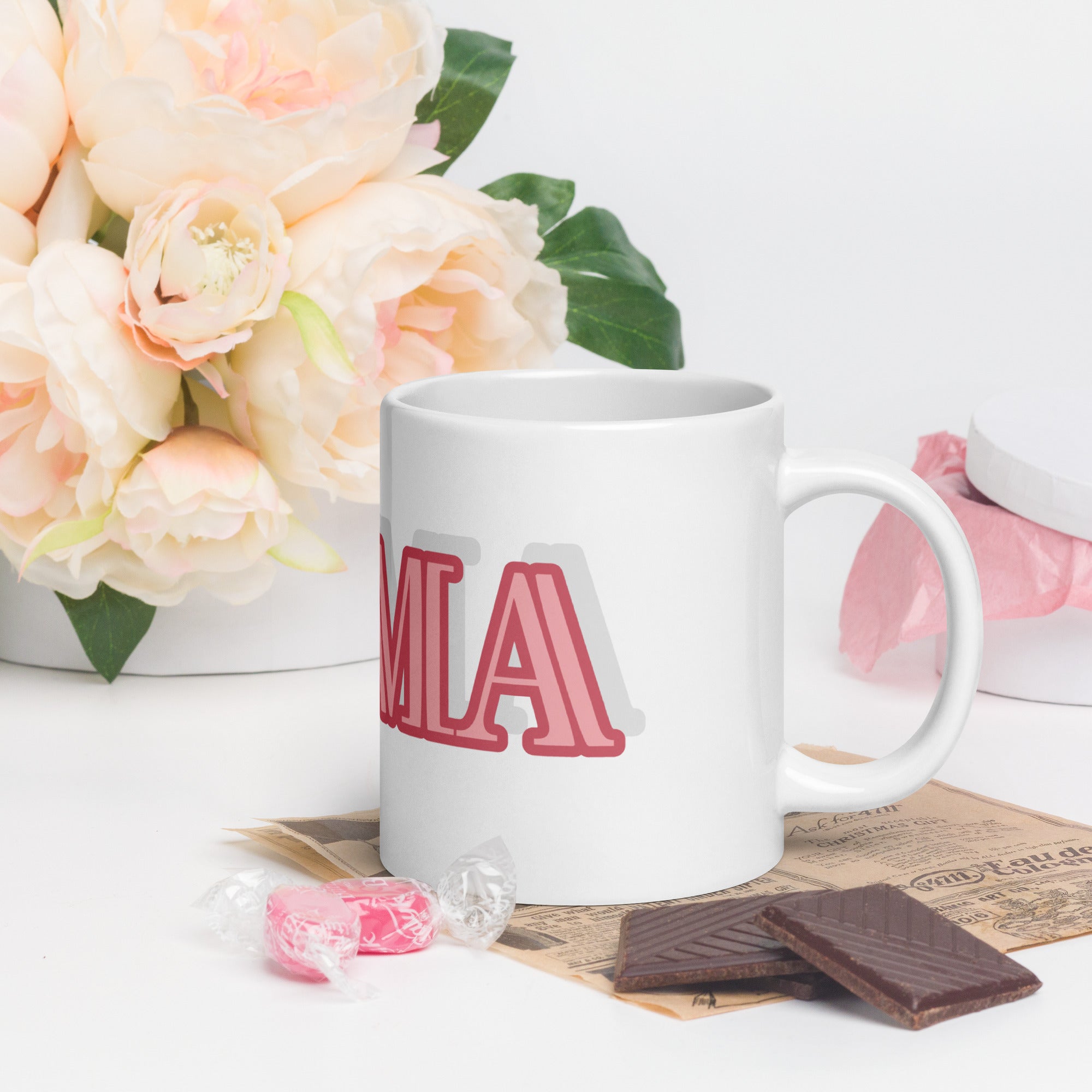 LuckeLadybug glam ma coffee mug with pink lettering on white ceramic mug beside flowers and chocolates