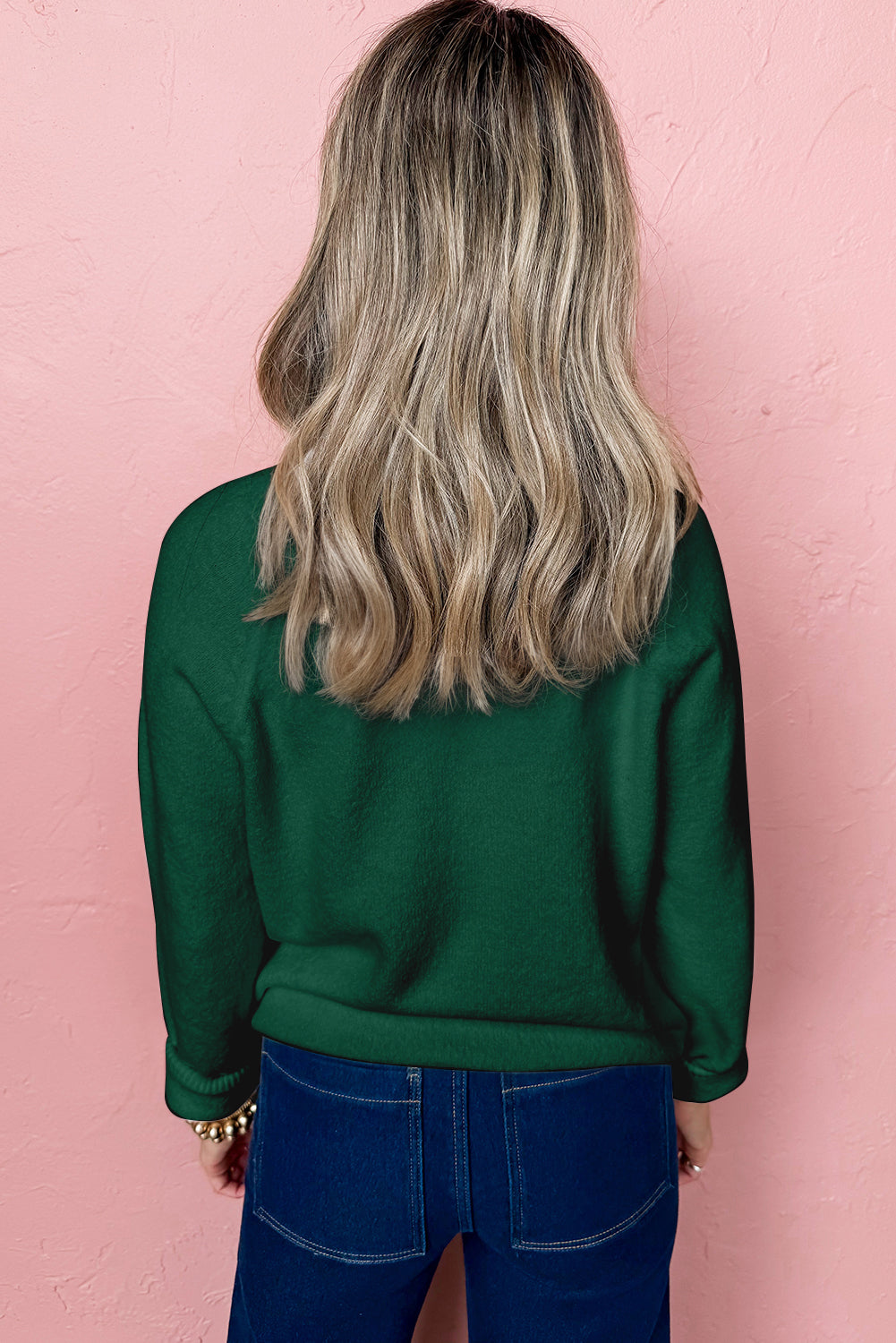Back view of a green sweater worn by a model featuring a white MERRY Christmas sweater design