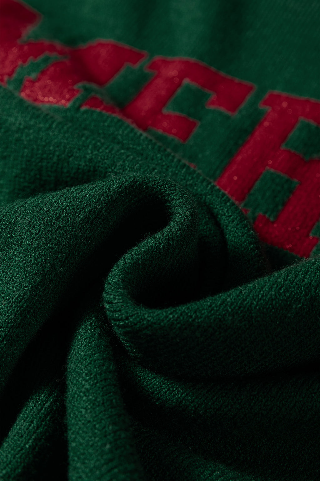 Close-up of a soft green fabric with red lettering of a white MERRY Christmas sweater by LuckeLadybug