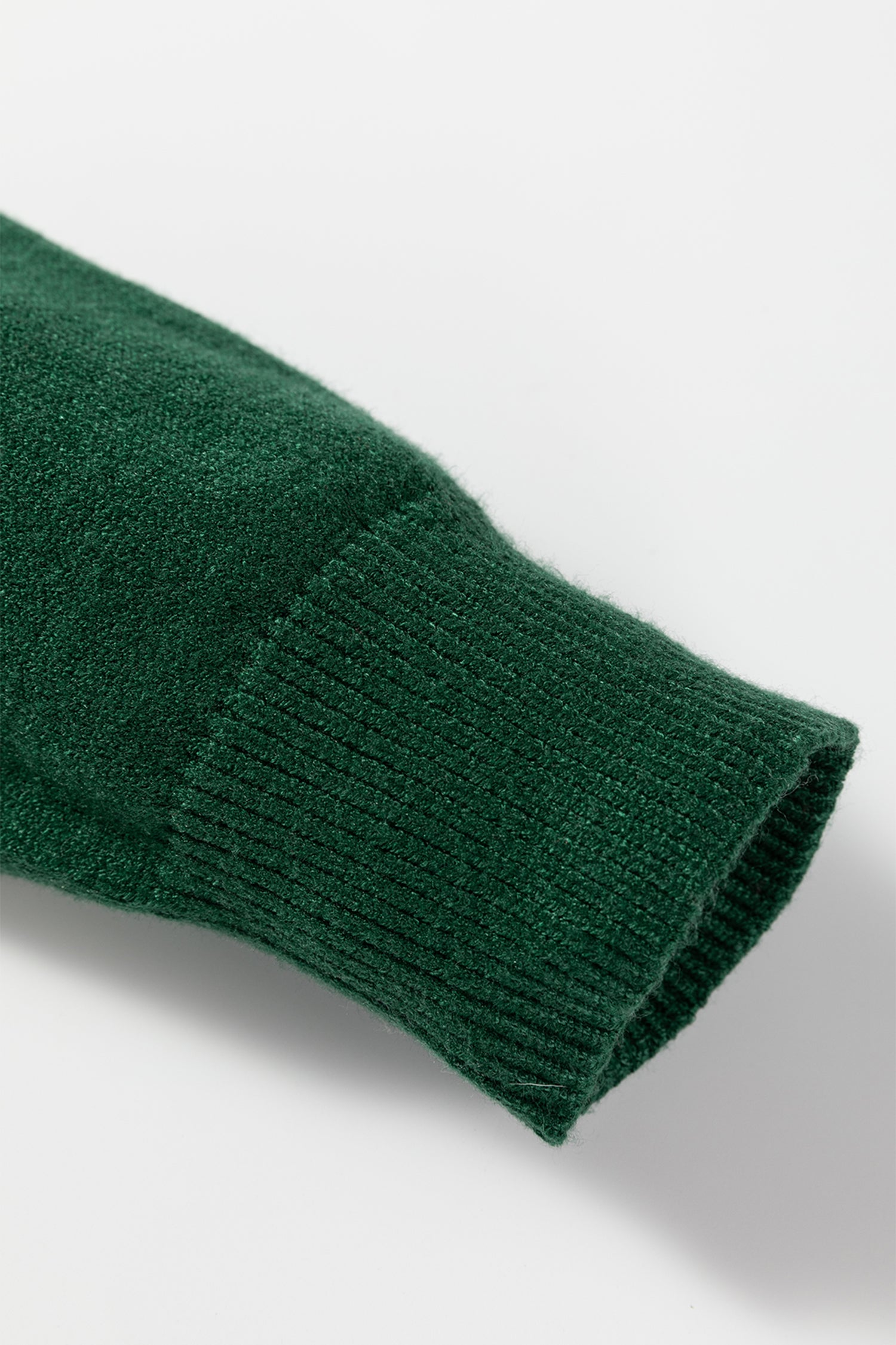 Close-up of a green sweater cuff, showcasing the cozy knit texture of the white MERRY Christmas sweater