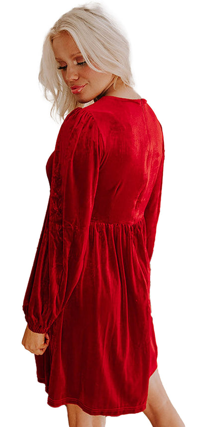 Blonde model wearing a fiery red velvet mini dress with long sleeves and gathered waist by a fireplace and Christmas tree