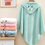Soft LuckeLadybug LLC hooded newborn towel in mint green with animal ears, hanging beside colorful stacked towels