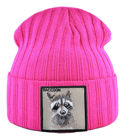 Pink knitted beanie hat with patch featuring an embroidered raccoon design