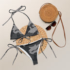Camouflage string bikini for women in shades of gray laid flat with round straw bag and sunglasses