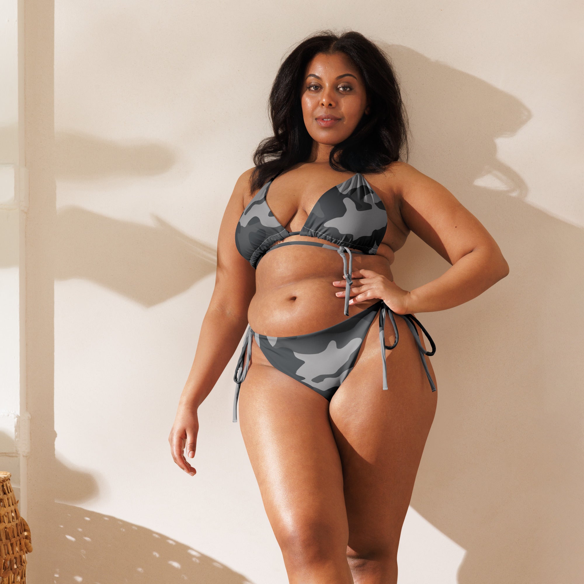 Curvy woman wearing a gray camouflage string bikini for women posing indoors against a light wall