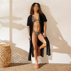 Woman wearing a leopard print string bikini and black sheer cover-up standing indoors by wicker furniture
