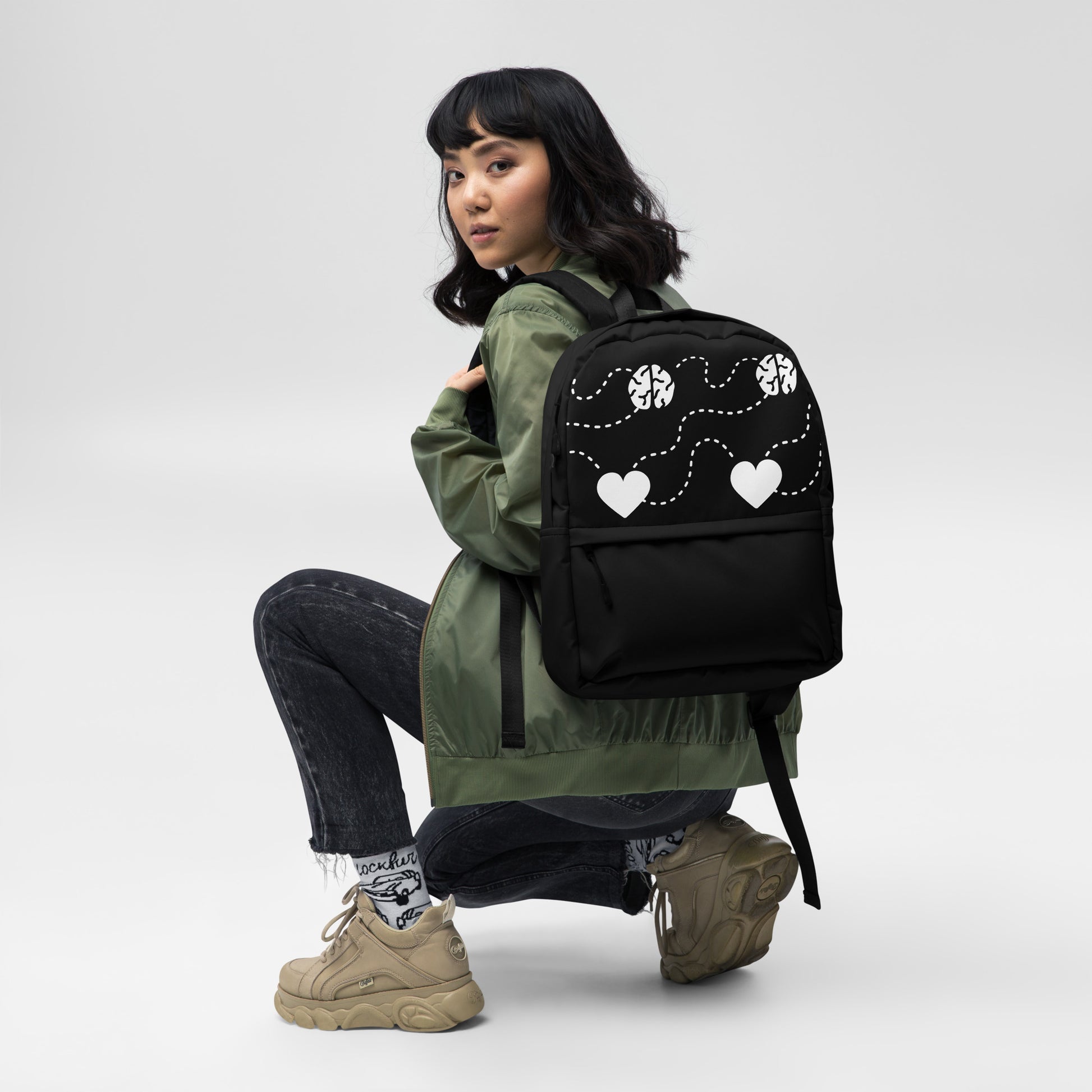 LuckeLadybug Black Backpack With White Hearts on model wearing green jacket heart pattern and front pocket