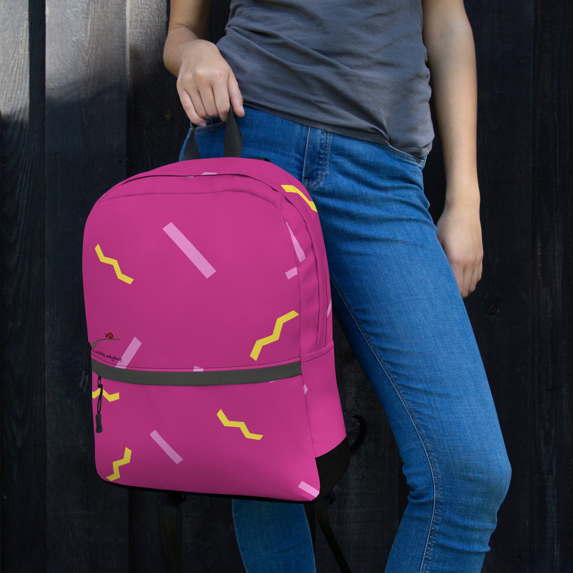 LuckeLadybug stylish school backpack in pink with yellow and light pink abstract patterns held by person wearing blue jeans