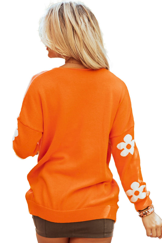 Back view of an orange floral knit cardigan with white flower details on the sleeves