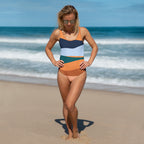 Woman wearing an orange stripe one-piece swimsuit standing on the beach with ocean waves in the background