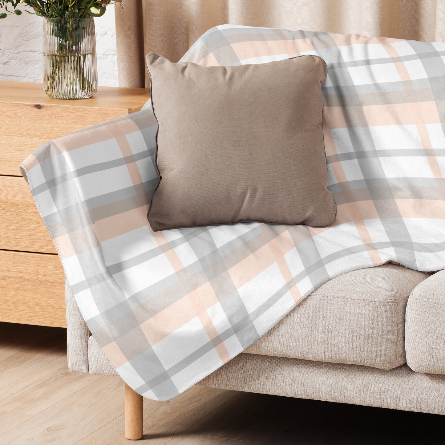 Peach grey plaid sherpa blanket draped over beige sofa with taupe pillow in cozy living room