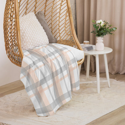 Peach grey plaid sherpa blanket draped over a wicker hanging chair with cushions in a cozy living space